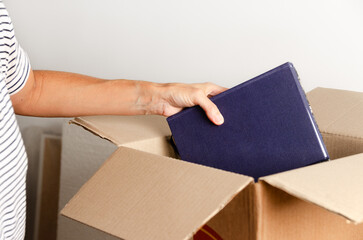 A woman's hand putting books into a cardboard box. 