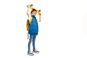 Full length photo of a happy blonde boy holding yellow longboard over head on white background. Back to School