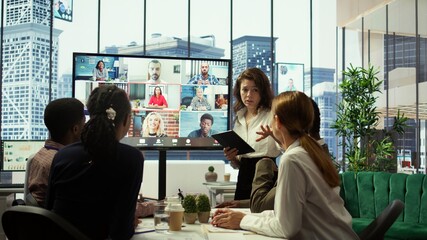 Business team in a boardroom attend videocall meeting with investors group, discussing about increasing funds for a global development plan. Staff and shareholders on teleconference. Camera B.