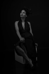 Black and white portrait of beautiful curly woman sitting on a cube