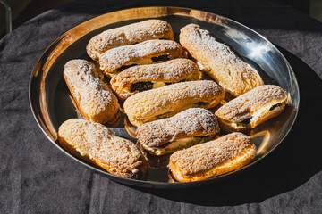 A plate of golden éclairs dusted with powdered sugar, filled with cream and blackberries