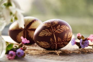 Brown Easter egg dyed with onion skins with a pattern of fresh leaves with spring flowers