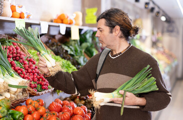 Adult man buyer choosing fresh green onions in vegetable shop