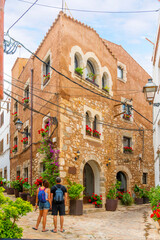 A man and woman traveling with backpacks stop to look at a stone building on an alley corner in the historic old town of Tossa de Mar, Spain.