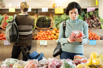 Woman carefully selects red bell peppers in a grocery supermarket