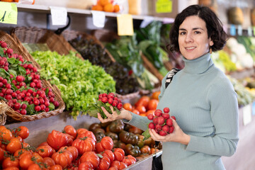 Adult woman buyer choosing fresh radishes in vegetable shop