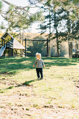 Naklejka premium Little girl stands on a green lawn in the park near the playground