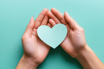 Obraz premium Hands gently holding a mint-green heart-shaped cutout against a soft teal background