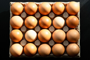 Cardboard tray containing twenty chicken eggs on a black background. Two dozen eggs. Top view