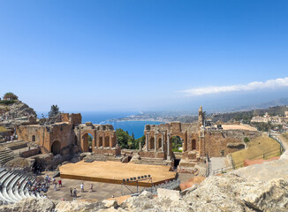 Taormina, Sicily, Italy - July 5, 2024: Ancient Greek theatre or Teatro antico. Wide landscape view down from the north with stage and backstage ruins as center, Blue sea and coastline on horizon. Peo