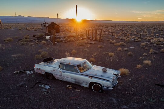 A vintage Cadillac sits abandoned in the Nevada desert, USA, at sunset. The car's faded paint and broken windows tell a story of time and neglect.  Beatty, Nevada, USA