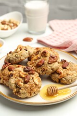 Tasty cookies with nuts and honey dipper on light table, closeup