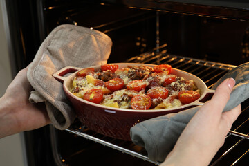 Woman taking delicious pasta casserole with cheese, tomatoes and minced meat out of oven, closeup