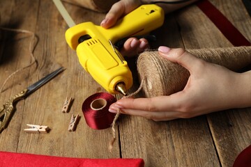 Woman with hot glue gun making craft at wooden table, closeup