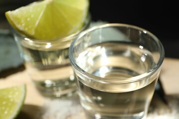Tequila shots and slices of lime on table against black background, closeup