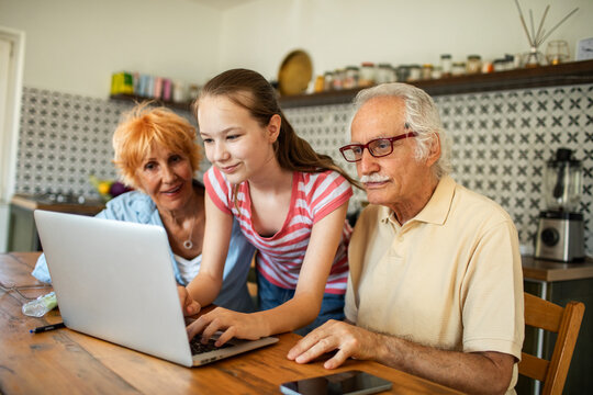 Grandparents helping granddaughter with laptop at home kitchen table