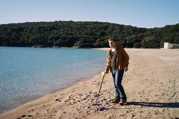 Beach cop swipes a metal detector across the sand while walking