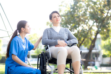 Fototapeta premium Young caucasian nurse comforting with patient while sitting on wheelchair in outdoor park, doctor woman support and counseling with patient, caregiver and service, medical and consoling.