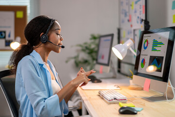 A woman wearing a headset is talking on a phone while sitting at a desk with a c