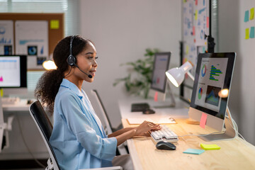 A woman wearing a headset is sitting at a desk in front of a computer monitor