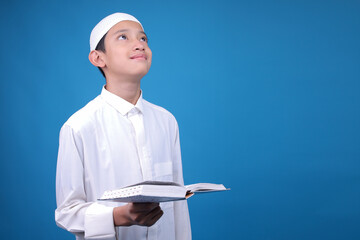 Smiling Young Muslim Man Reading Qur'an While Looking at Camera Isolated on Beige Background