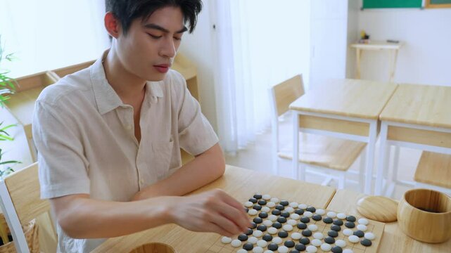 Asian young man playing board game Go during competition in community. 