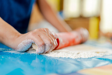 Chef using rolling pin, kneading dough on floured surface