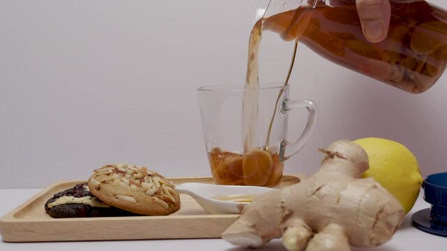 Hand of man pouring hot ginger tea, served with almond cookies, dark cookies, afternoon tea