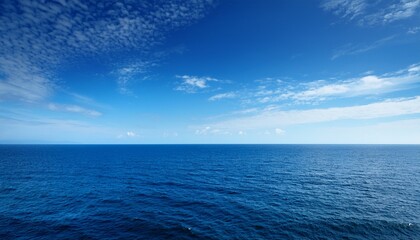 Fototapeta premium the vast expanse of the ocean stretches out before a clear blue sky dotted with wispy white clouds