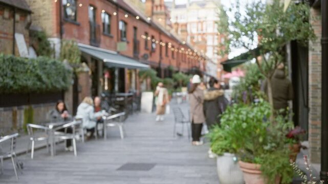 Blurred winter street scene in london with people walking and sitting at outdoor cafe tables in a charming urban setting with bokeh lights and red brick buildings.
