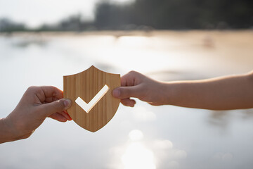 Image of two children's hands holding an insurance model in the shape of a shield with a check mark.