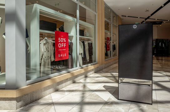 Background texture of a blank, sleek digital information board with copy space for a customized mockup stands prominently in a modern shopping center by retail clothing shops with discount sale signs