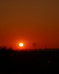 Glowing orange sunset over industrial skyline with drifting smoke