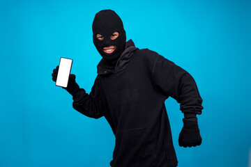 Evil Burglar Wearing Mask Showing Smartphone While Walking Isolated On Blue Background