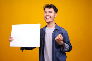 Positive Casual Man Celebrating Victory With A Blank Sign Board Isolated On Yellow Studio Background