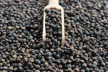 Black peppercorns ( Black pepper ) seeds on wooden shovel spoon with black peppercorns background. Food ingredients. Aromatic spice