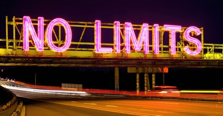 Neon sign no limits vibrant magenta yellow mounted metal structure highway glowing night blurred car lights rushing past