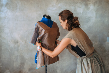 A woman fashion designer standing next to a mannequin, she is creating a dress from a piece of fabric, modeling it with a needle and making chalk marks for cutting. Atelier. Startup custom clothing.