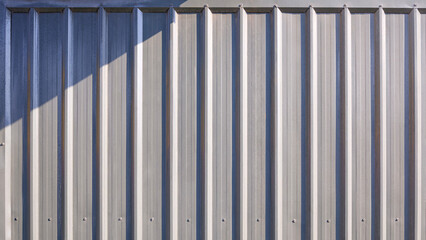 Gray corrugated metal exterior wall background of warehouse building or cargo container with light...