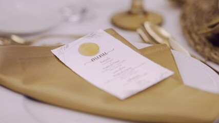 Close up of a wedding menu card placed on a folded golden napkin atop a white plate