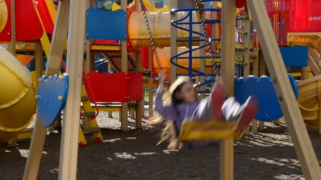 little girl plays on the playground, climbs the ladder labyrinths, slides down slides against the backdrop of multi-story buildings. Modern play space in a metropolis. family new buildings children