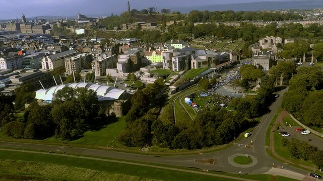 A stunning aerial view of Edinburgh, Scotland, showcasing the Scottish Parliament, Holyrood Palace, and lush green landscapes captured by drone on a sunny day.