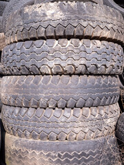 A stack of used tires with visible tread patterns, some dirt, and signs of wear. They are piled...