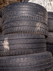 Obraz premium A stack of used tires with visible tread patterns, some dirt, and signs of wear. They are piled outdoors, likely for recycling or repurposing.