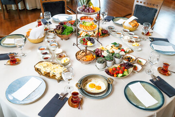 Fototapeta premium Classic Turkish breakfast in luxury restaurant. Delicious Turkish breakfast served on a round table with fried eggs, fruits, vegetables and drinks. Wide angle photo.Turkey.