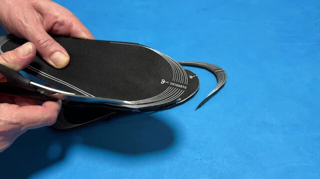 Close-up of a man's hands cutting electrically heated insoles to the correct size for a teenager with scissors. Warm warming insole with pre-installed heat elements perfect for winter walks.