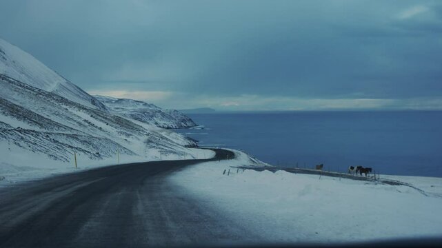 A winter highway in Iceland, flanked by snow covered fields, stretches toward a distant mountain range