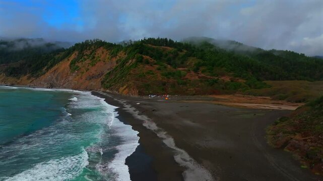 Sunny clear blue skies misty rugged surf rocky mountainside cliffs bluffs untouched remote USAL Beach campground California aerial drone camping Sinkyone Wilderness Lost Coast Trail forward up motion