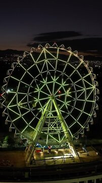 Vertical drone shot orbiting the ferris wheel of Aztlan Park, night in CMDX