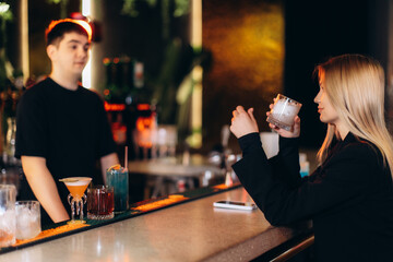 Young Woman Enjoying Drink at Bar with Bartender in Background